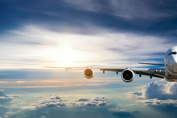 Half view of a commercial passenger aircraft flying above the clouds at sunset. Travel and holiday concept.