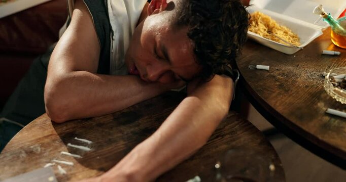 Overdose, addiction and man on table with drugs, powder and healthcare danger with narcotic abuse. Mental health, sleeping and tired person with cocaine lines, fentanyl risk and opioid crisis in home