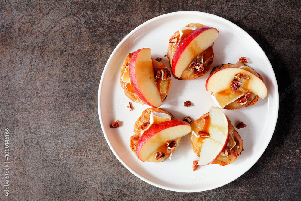 Poster plate of crostini appetizers with red apples, brie cheese and walnuts. overhead view against a dark 