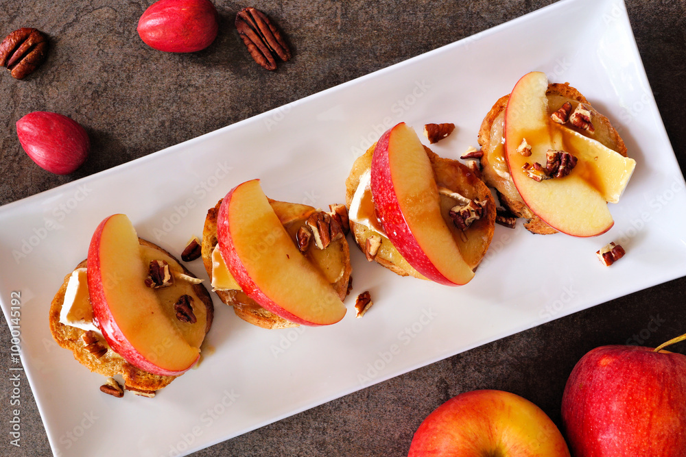 Poster crostini appetizers with red apples, brie cheese and walnuts. above view table scene against a dark 