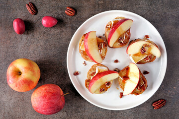 Plate of crostini appetizers with red apples, brie cheese and walnuts. Top view table scene against a dark background. Party food concept.