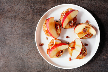 Plate of crostini appetizers with red apples, brie cheese and walnuts. Overhead view against a dark background. Party food concept.