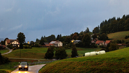 A car drives through the rain on the road in Schweigmatt in the Black Forest in the evening with...