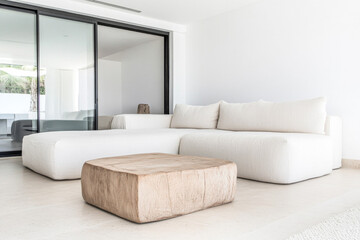 Modern minimalist living room with white sectional sofa and wooden coffee table, featuring large windows for natural light
