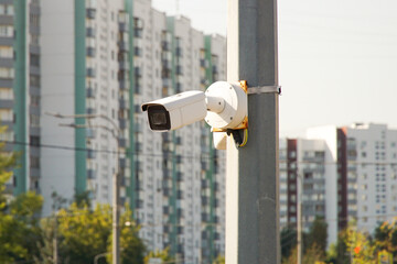 CCTV camera mounted on a pole against the backdrop of a modern building and trees.