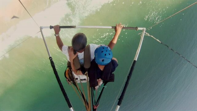 Aerial view of two people hang gliding over the ocean. The gliders are in motion, soaring above the sparkling water, capturing the essence of adventure and freedom in the sky