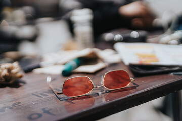 Close-up of stylish sunglasses resting on a wooden table with blurred objects in the background, highlighting a relaxed and casual atmosphere.