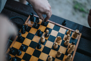 Close-up of hands strategically moving chess pieces on an outdoor wooden chessboard, capturing the...