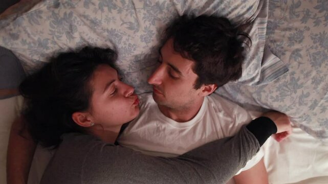 Couple lying together in bed, sharing a tender and loving gaze. The moment captures a sense of intimacy and warmth in a cozy bedroom setting