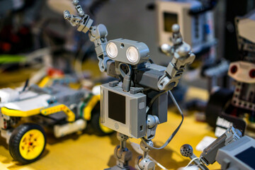 Detailed view of a toy humanoid robot built from construction blocks, with blurred robotics parts in the back