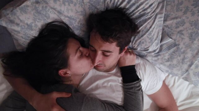Couple resting in bed, the woman softly embracing the man. A tender moment of comfort and closeness in a serene, peaceful bedroom setting