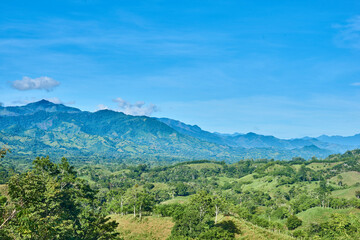 green mountain range with blue sky and clouds, hillocks with green trees