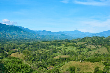 Obraz premium Green mountain range with blue sky and clouds, hills with trees, abundant vegetation and grass of different shades