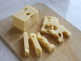 A block of maasdam cheese and sliced pieces on a wooden board on a white background. Dairy products, cheese making. Maasdam and radomer - cheese with big holes