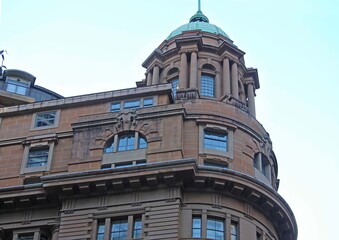 The top front corner of an old rounded sandstone building. Domed roof with columns and arched windows.