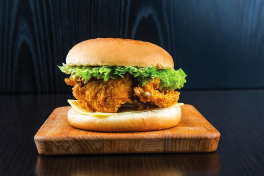 Chicken Zinger Burger with Lettuce, Tomato, Melted Cheese and Sauce isolated on wooden board side view of fastfood on dark background