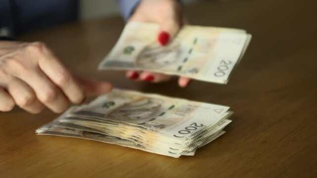 Female hands counting 200 polish zloty bills at the table - banking, business, and finance concept, close-up shot