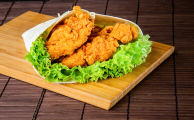 Crispy Chicken Zinger Wrap with Lettuce and Tomato isolated on wooden board closeup side view of fast food on dark background