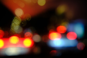 Defocused Rain shower on car windshield or car window and blurry road lights in background. Driving in rainy season. Rain drops on car mirror. Traffic road in evening rain. 