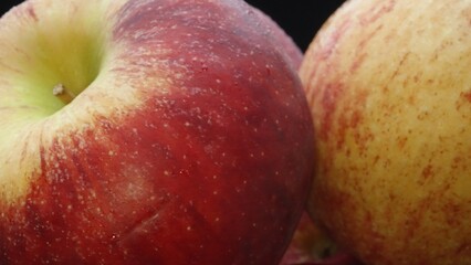 Close-up showcases a crisp bright red fresh apple nestled comfortably in a glass bowl. The black background creates a dramatic stage, highlighting the apple's flawless and smooth skin. Comestible.