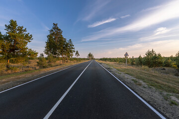 A long, empty road with a few trees in the background