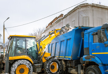 A yellow and blue construction vehicle is parked next to a blue dump truck