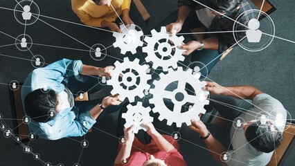 Top view of professional business people joining and gathering wooden gear together. Aerial view of diverse team working together to put or collect cog with network connection holographic. Symposium.