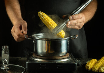 Cooking boiled corn in a pot in a restaurant kitchen. The chef takes out a hot head of corn with tongs.