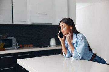 Woman sitting at kitchen counter in modern home talking on cell phone, staying connected in the digital age