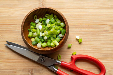 Wooden bowl with cut green onions on a cutting board