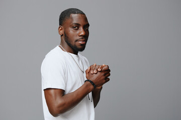 Stylish young man in casual white shirt with hands clasped, looking confidently at the camera against a neutral gray background Modern fashion portrait capturing a relaxed vibe