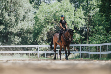 A young woman in a riding helmet and black attire riding a horse in an outdoor arena, enjoying an equestrian activity on a sunny day.