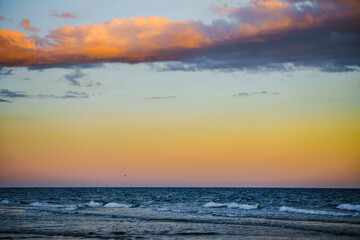 Vibrant sunset sky over the ocean with soft waves and colorful clouds.