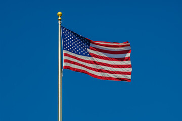 Obraz premium American Flag Waving on Flagpole Against Clear Blue Sky