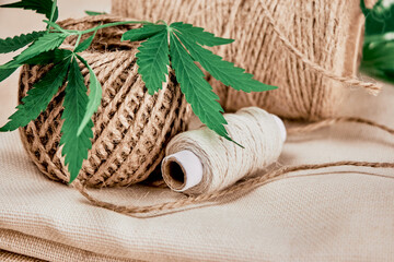 skein, ball and spool of natural hemp fiber threads with green cannabis leaf are on hemp fabric...