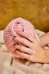 girl holding a skein of pink yarn in her hands to do her hobby in a cozy home atmosphere