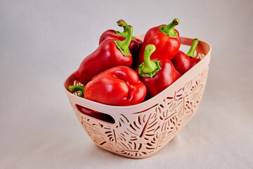 textured beige basket filled with red sweet bell peppers, paprika on a light background close-up, healthy and proper nutrition concept