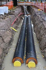 Two large insulated pipes are visible in a trench filled with water, likely part of a district heating or water distribution system