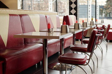 Vibrant retro diner showcasing shiny red vinyl booths and chrome tables. Condiment dispensers adorning each table, with stainless steel accents and geometric wallpaper complementing surroundings