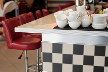 Grouping white cups neatly on counter near red bar stools in modern coffee shop showing an organized setup