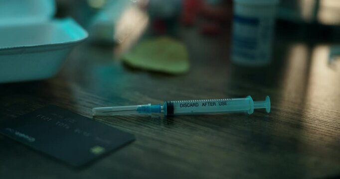 Drugs, addiction and syringe on dirty table with neon lights, card and narcotic injection at night. Danger, mental health and heroin needle with fentanyl risk, abuse and opioid crisis in messy home