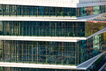 Fototapeta premium Modern office building with glass facade and green landscaping elements inside, reflecting the surrounding cityscape