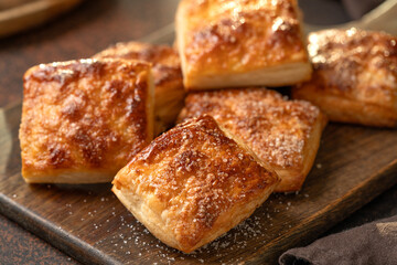 Puff cookies square with sugar on a serving board. Delicious homemade cakes on a dark background closeup