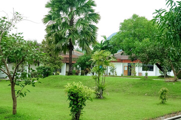 A serene villa surrounded by lush greenery, featuring a traditional yet modern architectural design with a sloping red-tiled roof. The villa is nestled amidst a garden landscape