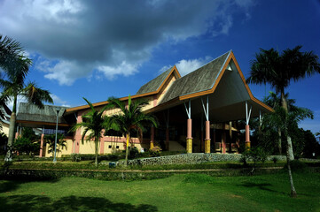 A serene villa surrounded by lush greenery, featuring a traditional yet modern architectural design with a sloping red-tiled roof. The villa is nestled amidst a garden landscape