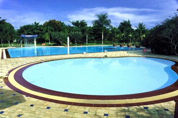 A serene swimming pool atmosphere, perfect for family vacations, featuring crystal-clear water, adorned with plants and a pavilion for relaxing and enjoying a sunny day