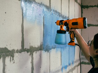 girl paints concrete wall blue with spray gun