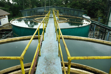 A Water Treatment with a walkway bridge leading to a series of large, circular water treatment tanks at an industrial facility. The yellow handrails on either side of the blue metallic walkway provide