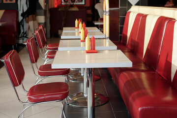Interior of retro diner showcasing rows of red leather seats and white tables with condiment bottles on each table, creating nostalgic ambiance