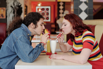 Two friends sharing milkshake at a retro diner, enjoying their time together. Decor filled with vintage elements and vibrant colors creating nostalgic atmosphere